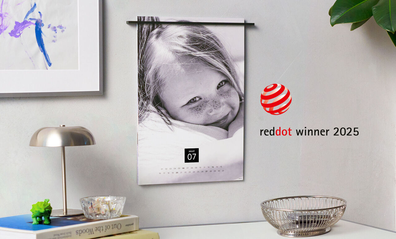 Immagine in bianco e nero di un bambino felice avvolto in una coperta. L'immagine è intitolata 'red dot winner 2025'.