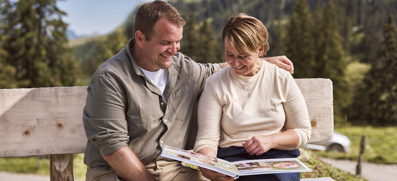 Una coppia guarda un fotolibro insieme su una panchina in natura.