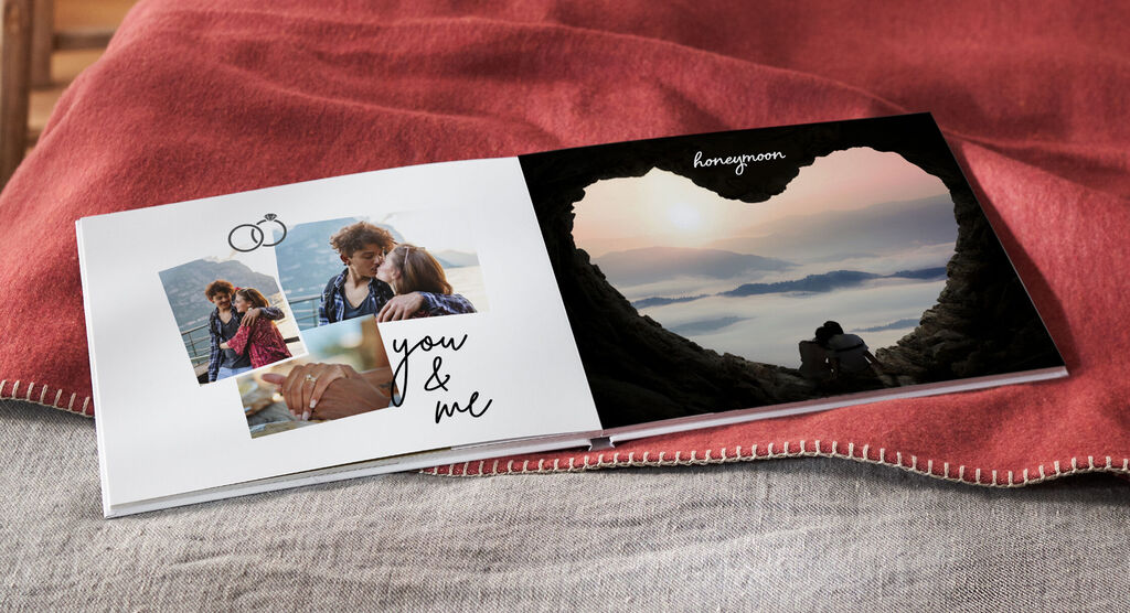 Un album fotografico aperto mostra momenti romantici di una coppia, circondati da un paesaggio a forma di cuore. CEWE ALBUM.