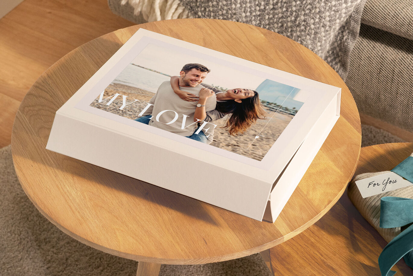 Una coppia sorridente sulla spiaggia. La copertina del fotolibro CEWE mostra la scritta 'MY LOVE'.