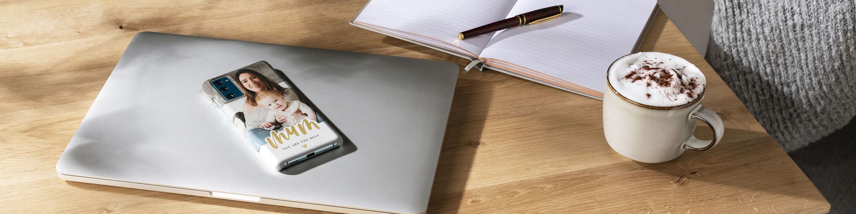 Una tazza di cioccolato accanto a un laptop su cui c'è un album fotografico CEWE.
