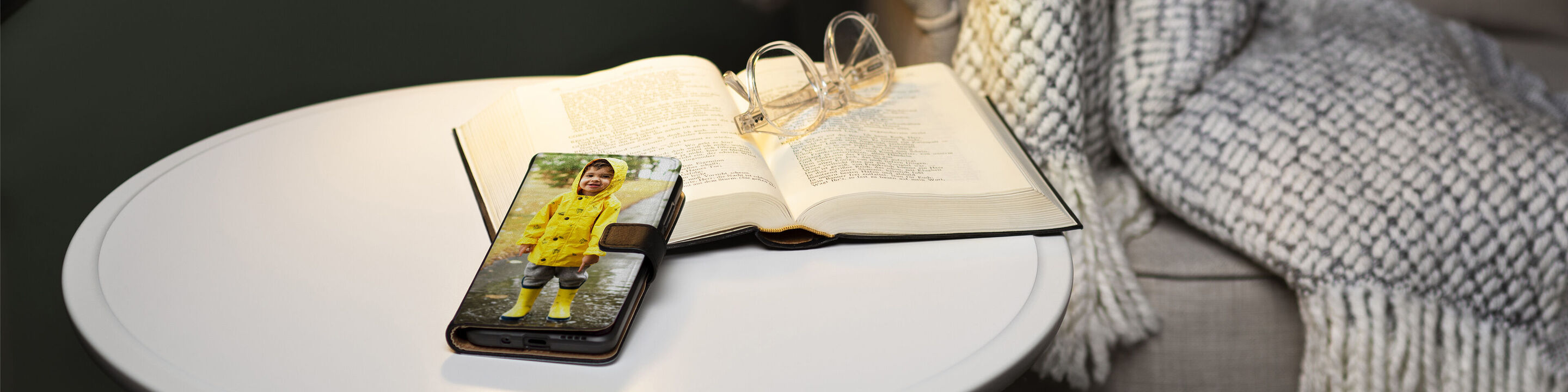 Uno smartphone con un'immagine di un bambino in un impermeabile giallo su un tavolo, accanto a un libro aperto e occhiali.