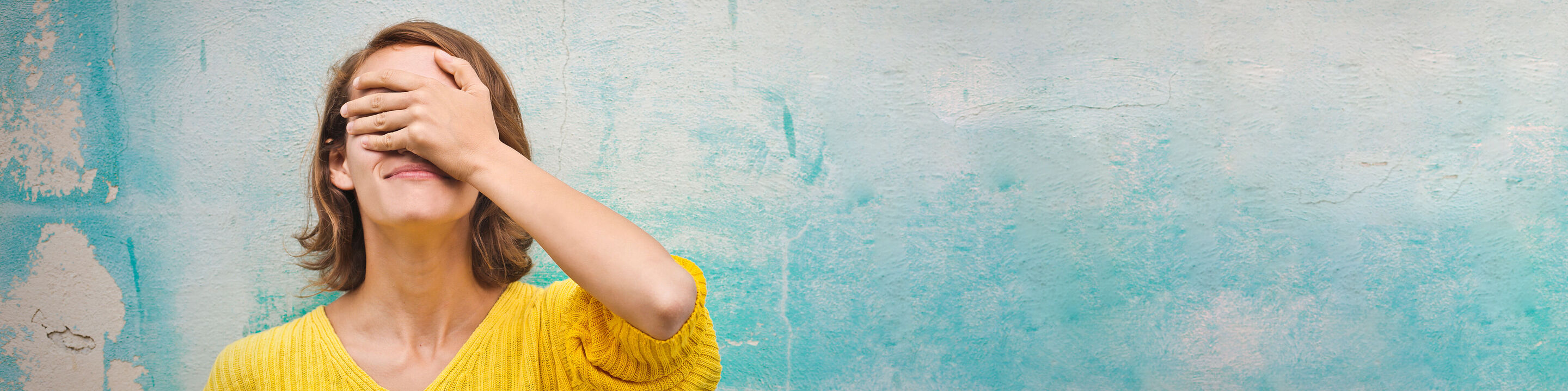 Una donna in un maglione giallo gode di un momento di tranquillità davanti a un muro blu.