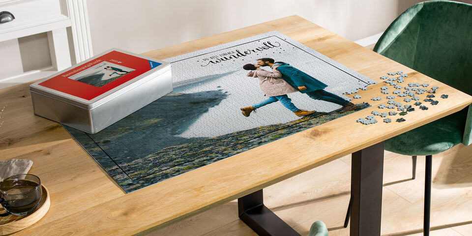 Una coppia si bacia davanti a un paesaggio composto da puzzle, con una scatola di puzzle accanto.