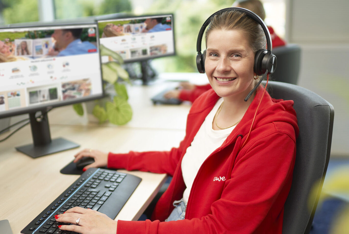 Una dipendente CEWE lavora al computer con auricolari per assistere i clienti.